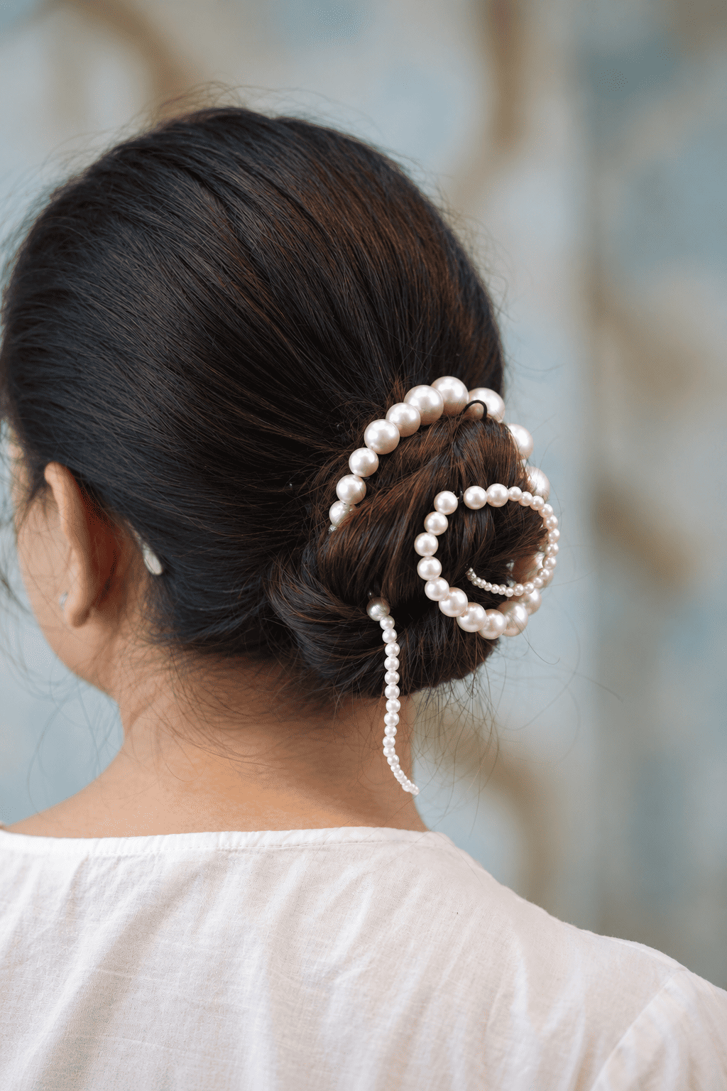 Back view of a brunette updo styled with a spiral ivory pearl bun accessory