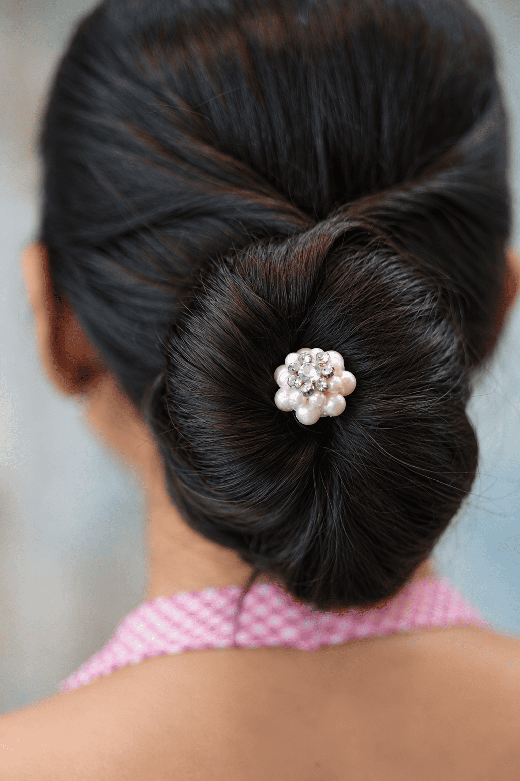 Close-up of an white pearl and clear crystal floral juda pin in a dark hair bun