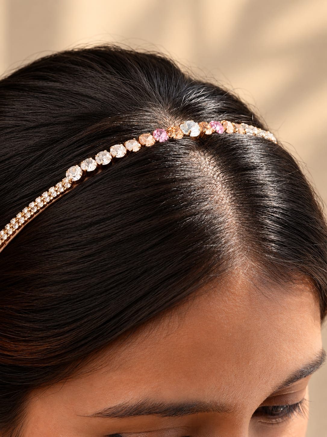 Close-up of a slim gold-tone headband embellished with pink and champagne crystal rhinestones