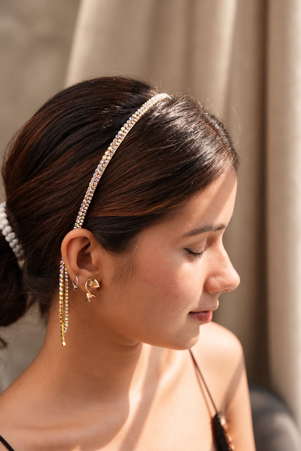 Woman wearing a gold-tone rhinestone headband with long dangling crystal tassels beside the face