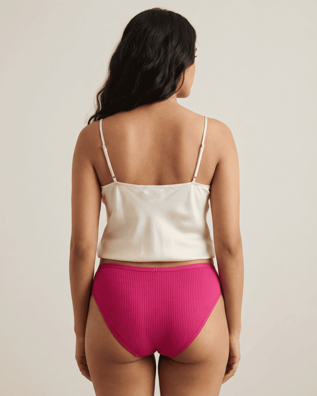 Woman wearing a white satin camisole and pink high-waisted underwear on a beige background