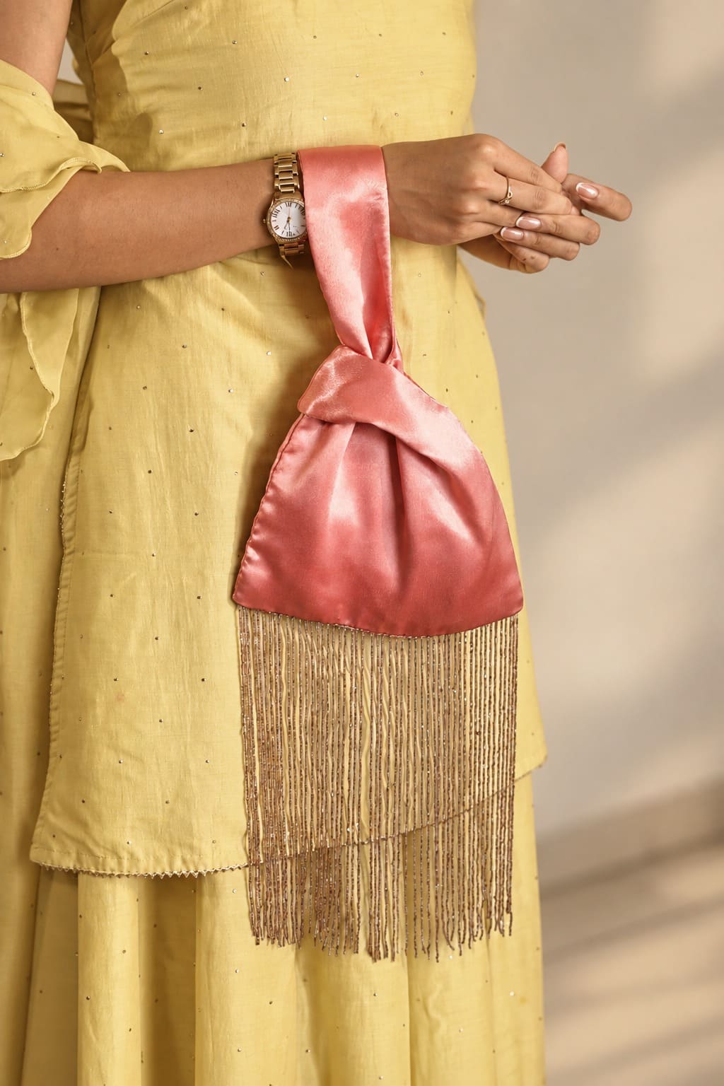 Dusty rose pink Japanese knot bag with long rose-gold-toned beaded fringe held against a yellow outfit