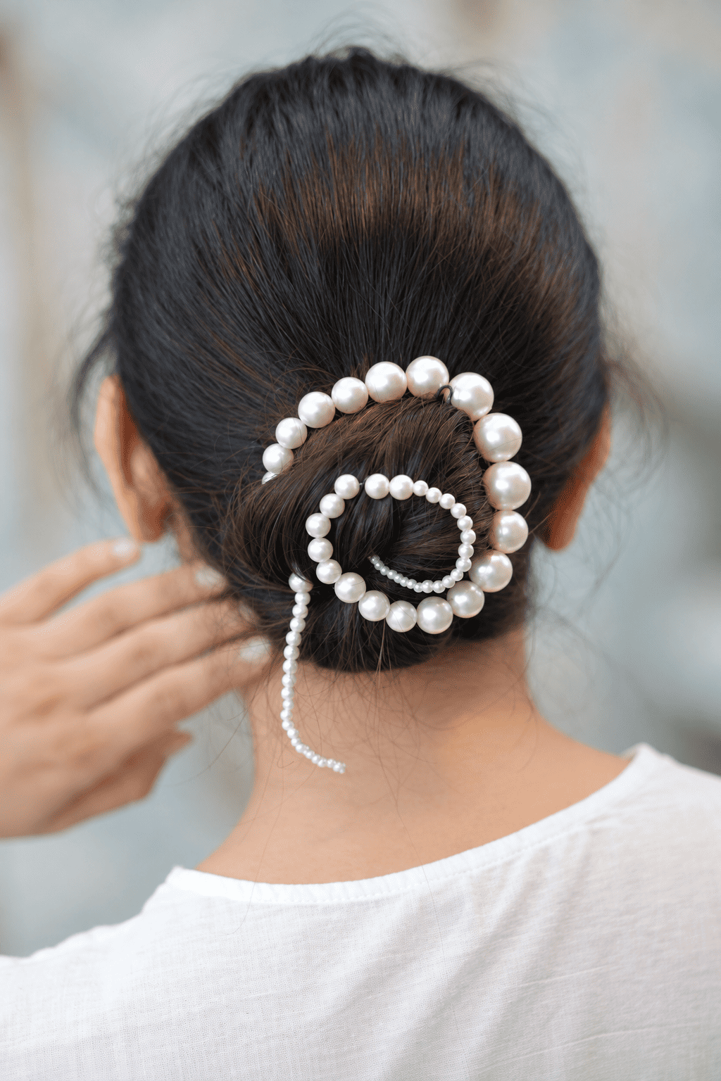 Pearl spiral hair bun accessory with a trailing pearl strand styled on a brunette bun
