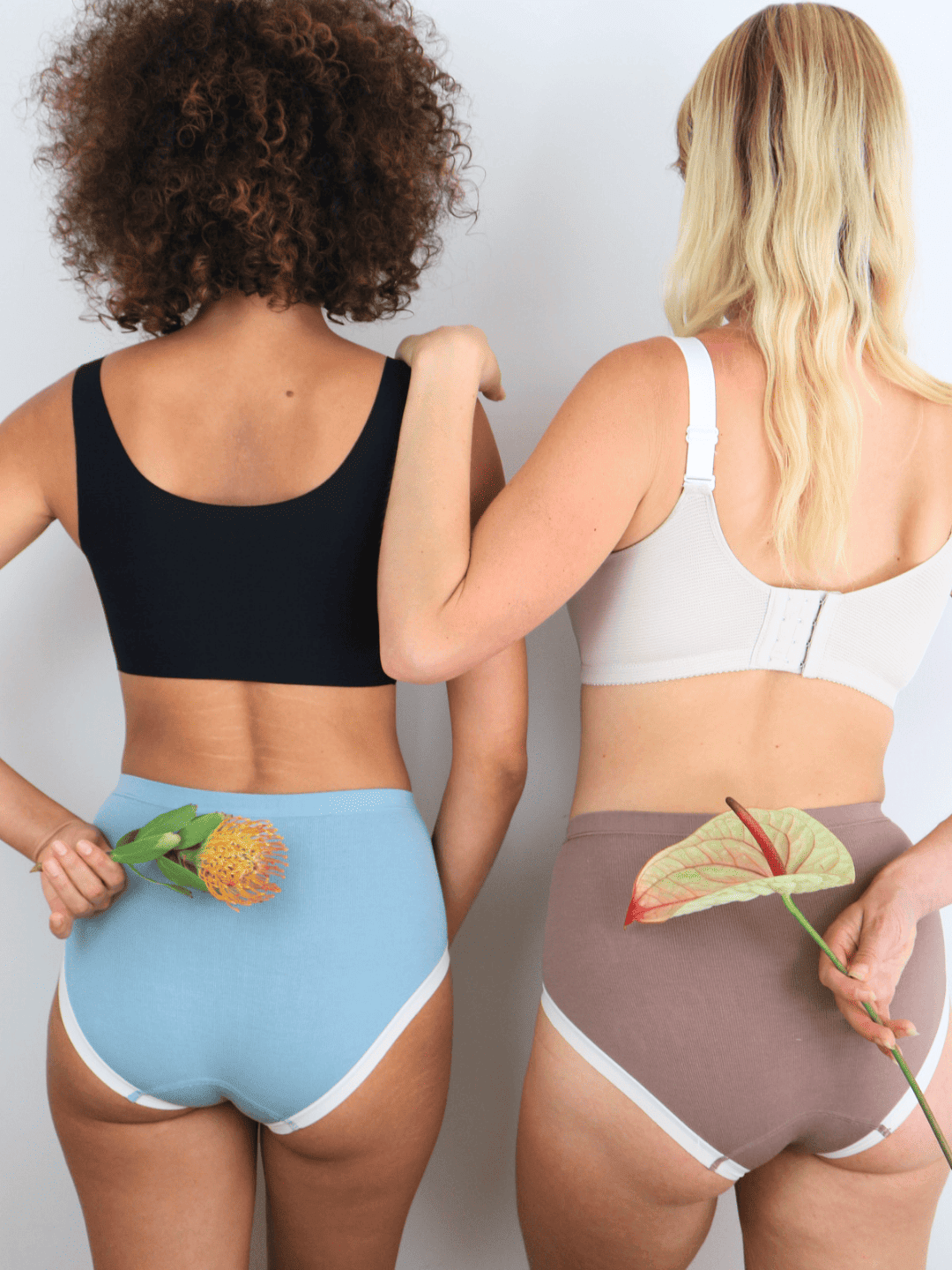 Two women wearing yew tree bae hipster underwear powder blue and brown color holding flowers on a plain background