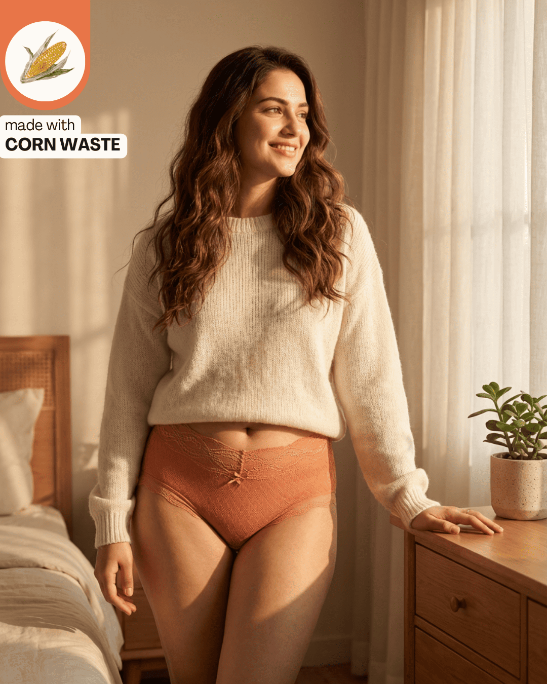 Woman wearing a white sweater and orange corn and lyocell high rise underwear standing in a bedroom with a corn waste logo in the corner.