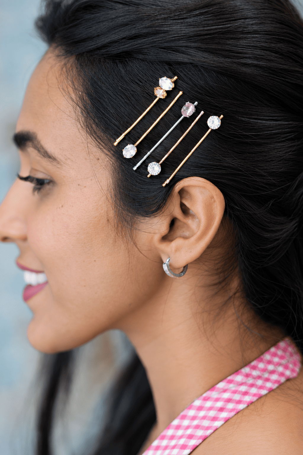 Side-profile view of a woman styling three geometric crystal hair clips stacked together in a side-swept elegant hairstyle for holiday party inspiration.