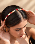 Top view of a model styling the IQ Edit Ruby Glow crystal rhinestone headband with red, clear, and champagne-toned gemstones on a sleek gold-tone band.