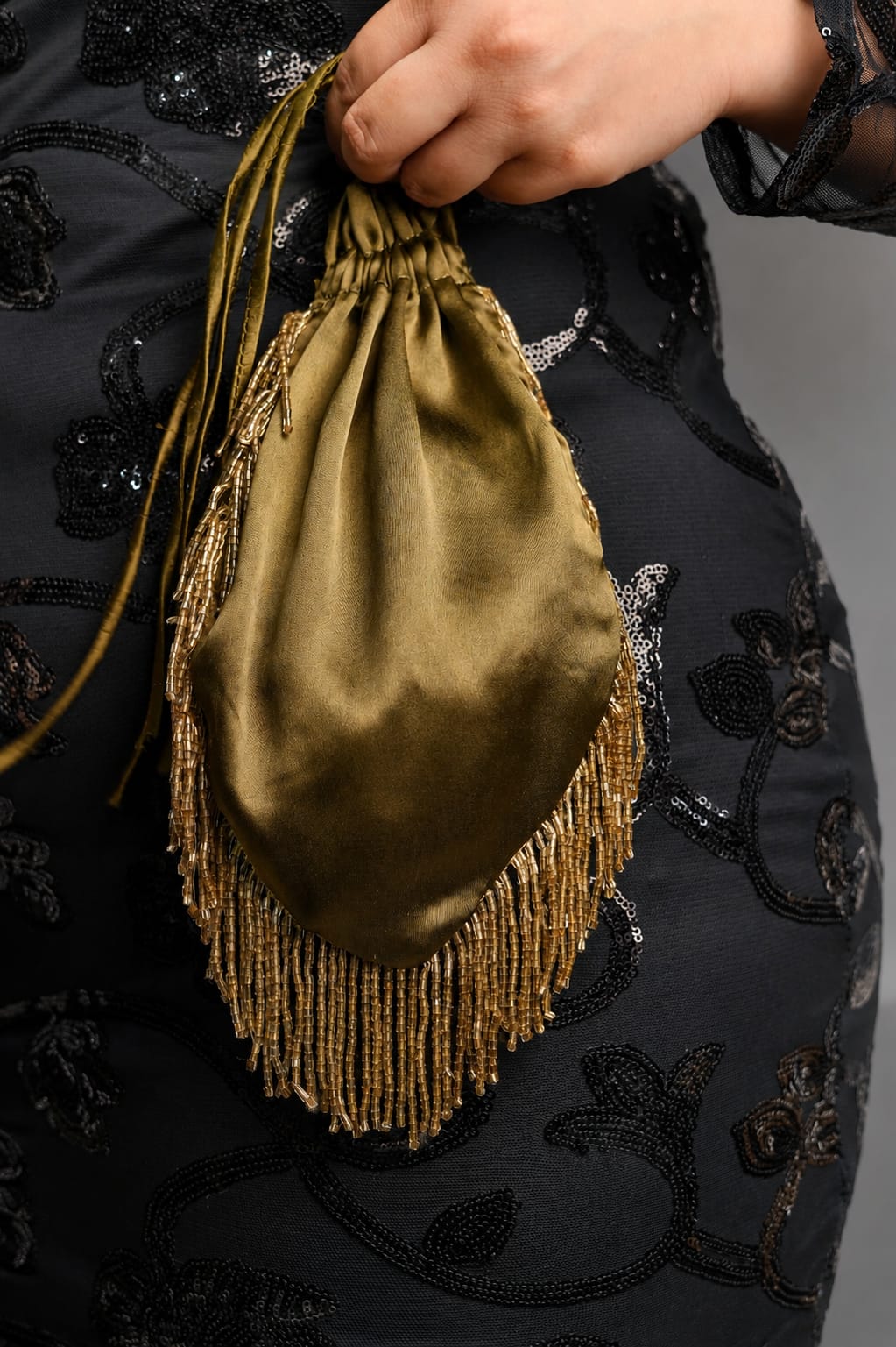 Olive green satin beaded fringe potli held by hand, showing its drawstring closure